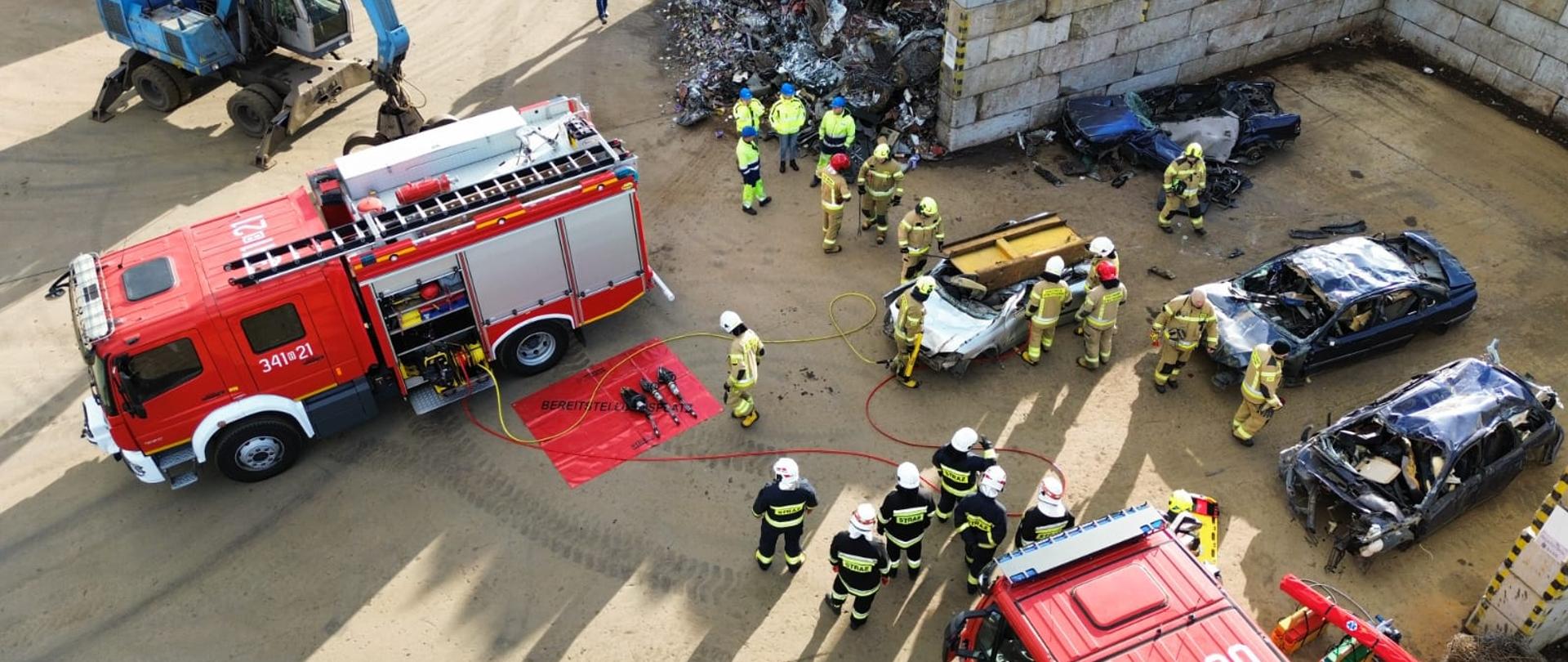 Ujęcie z drona, widać plac z wrakami pojazdów, samochody pożarnicze ustawione do ćwiczeń.