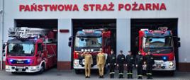 Widok z przodu. Zmiana służbowa na tle budynku jednostki i pojazdów, które częściowo stoją przed garażem. Dowódca salutuje. 