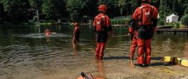 Strażacy podczas ćwiczeń wyciągają z wody poszkodowanego przy użyciu rzutki ratowniczej
