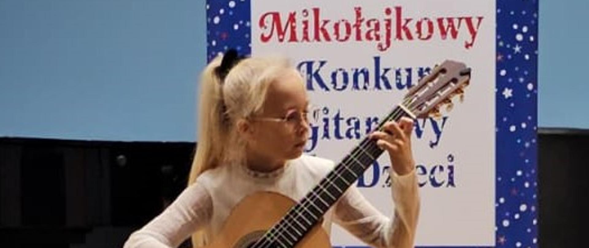 Zdjęcie Zuzanna Stach Rybik 2024 - uczennica grająca na gitarze, w tle baner reklamowy konkursu