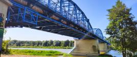 Zdjęcie z boku mostu, widok na filary posadowione w rzece i spód mostu pomalowany na niebiesko