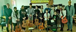 Zdjęcie przestawiające wszystkich uczestników popisu gitarowego, w tym nauczycieli - pana Bartłomieja Filipowicza i pana Sebastiana Środy, w auli szkoły w dniu 08.05.2023 r.