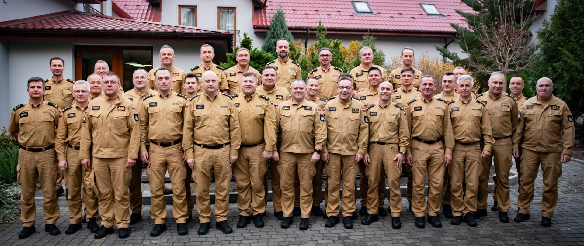 strażacy, uczestnicy szkolenia, pozują do zdjęcia grupowego na tle budynku