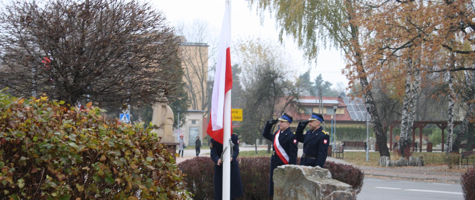 Poczet flagowy składający się z 3 strażaków podnosi flagę państwową na maszt 