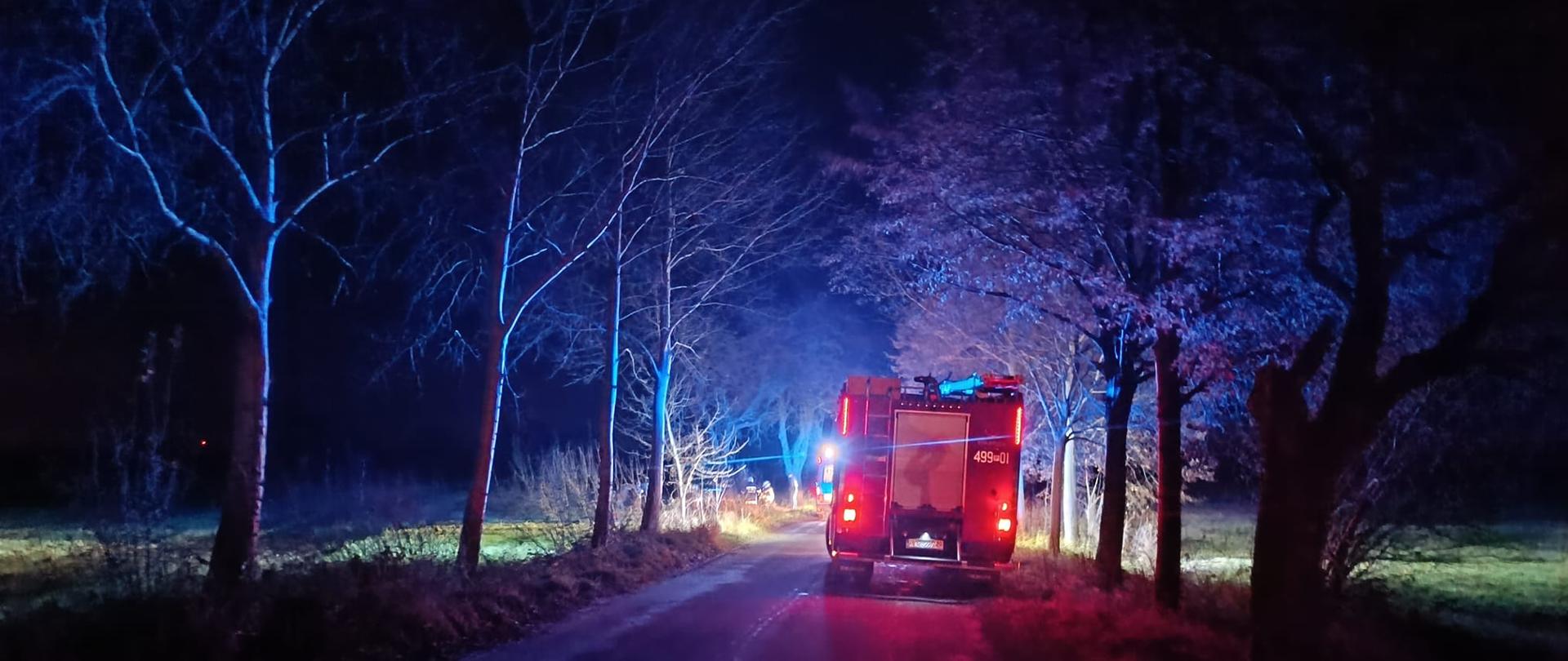 Zdjęcie przedstawia pojazd pożarniczy na drodze podczas prowadzonej akcji ratowniczej.