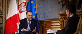 Minister Radosław Sikorski wziął udział w Naradzie Ambasadorów Republiki Francuskiej. Na zdjęciu szef polskiej dyplomacji udziela wywiadu, w tle flagi Francji, Polski i Unii Europejskiej.