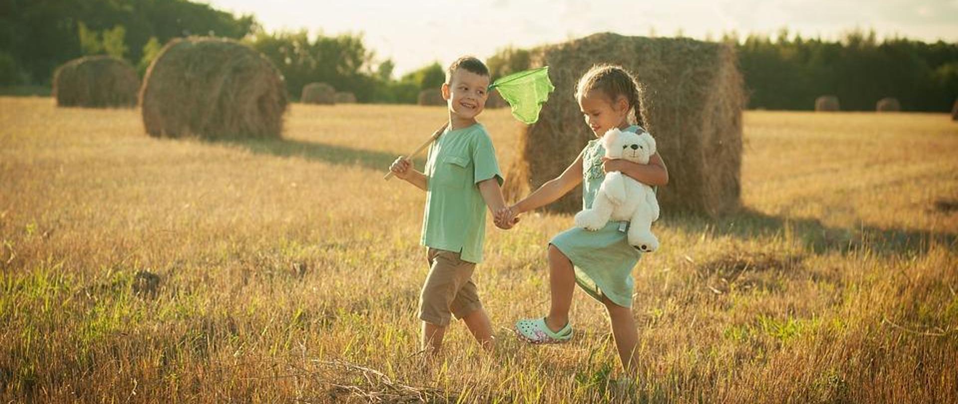 dwoje dzieci chłopczyk i dziewczynka idą przez pole trzymając się za ręce