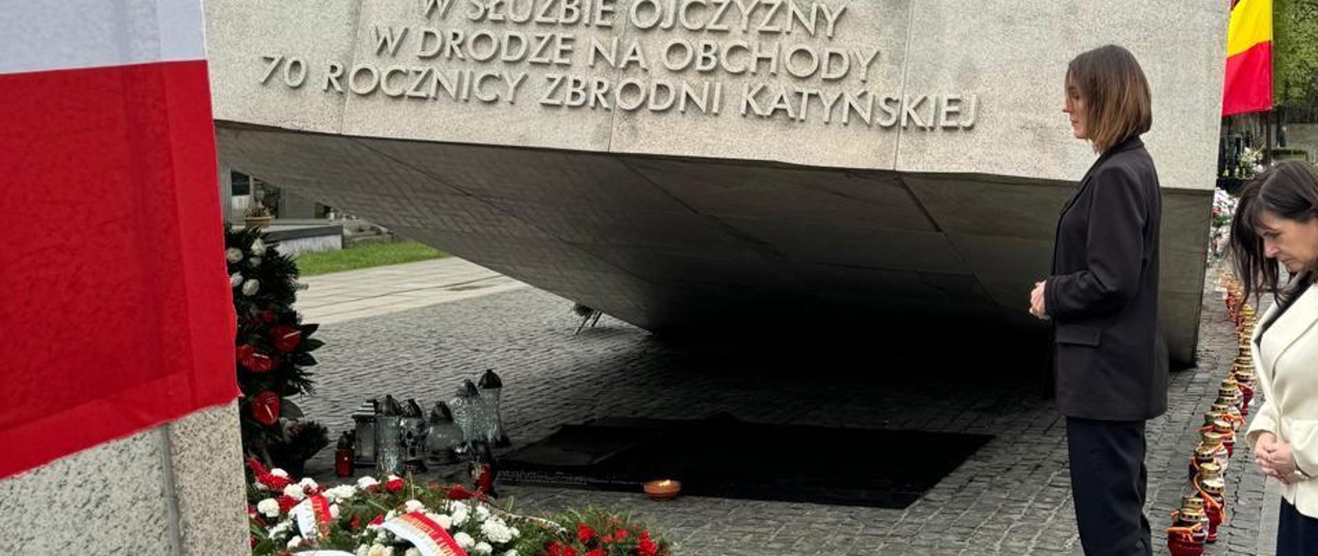 Wojewoda stoi przed pomnikiem ofiar katastrofy smoleńskiej, wokół mnóstwo biało czerwonych kwiatów i i flag
