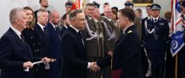 W przeddzień Narodowego Święta Niepodległości Prezydent Andrzej Duda wręczył w Pałacu Prezydenckim nominacje generalskie nadbryg. Pawłowi Kielarowi Opolskiemu Komendantowi Wojewódzkiemu Państwowej Straży Pożarnej. Prezydent RP ściska dłoń komendantowi. Obok Prezydenta stoi Minister Spraw Wewnętrznych i Administracji Tomasz Siemoniak, który trzyma pamiątkową szablę. Komendant Kielar trzyma w lewej dłoni czerwoną teczkę. Uroczystość odbyła się w Pałacu Prezydenckim.