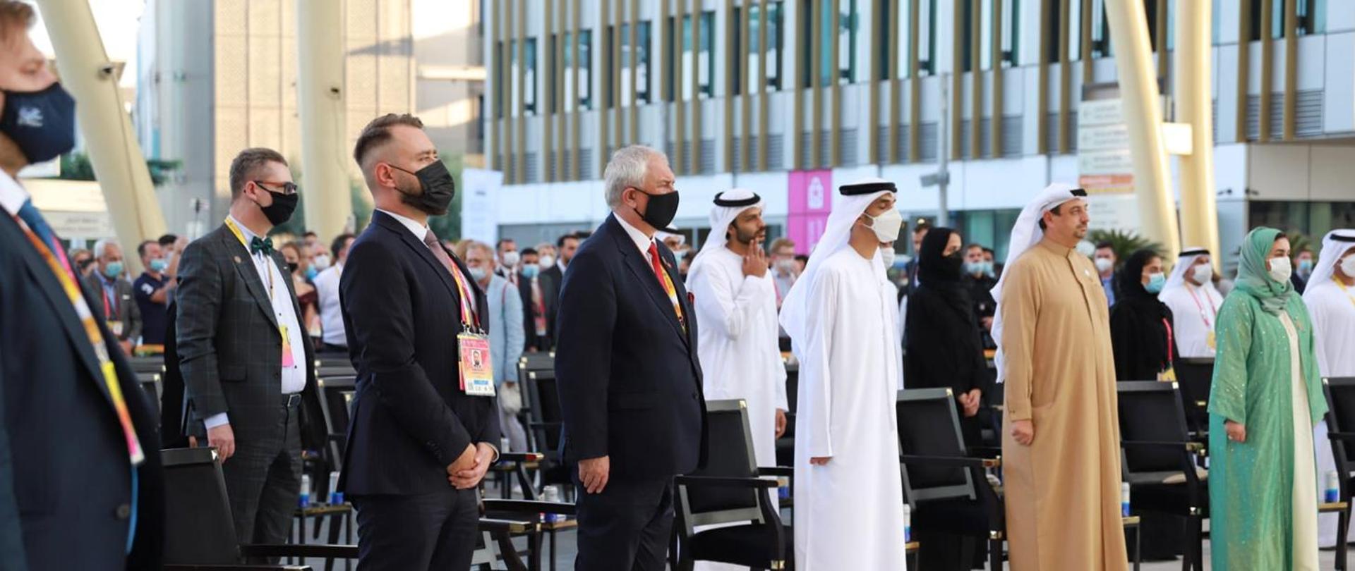 Deputy Minister Grzegorz Piechowiak stands at attention next to other people, including Dubai sheikhs.