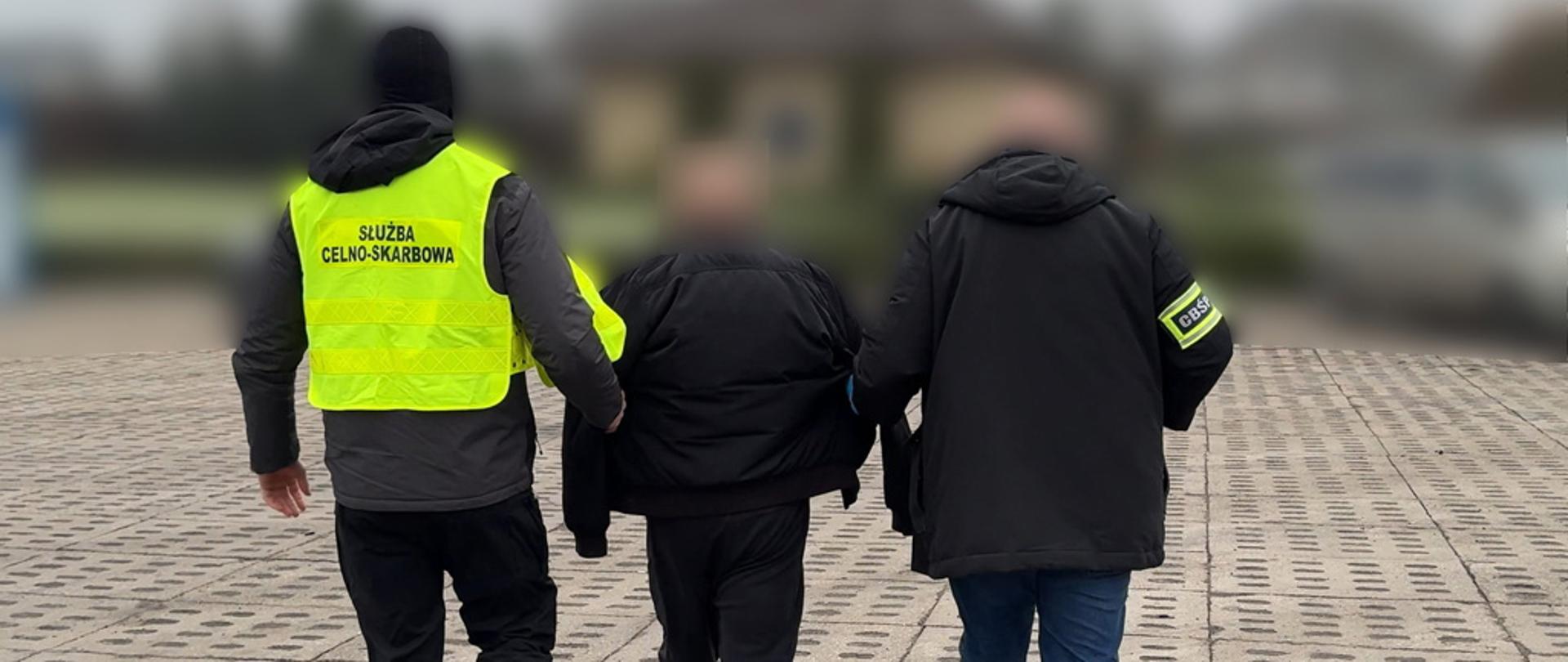 Funkcjonariusze Służby Celno-Skarbowej i Centralnego Biura Śledczego Policji prowadzą zatrzymanego.