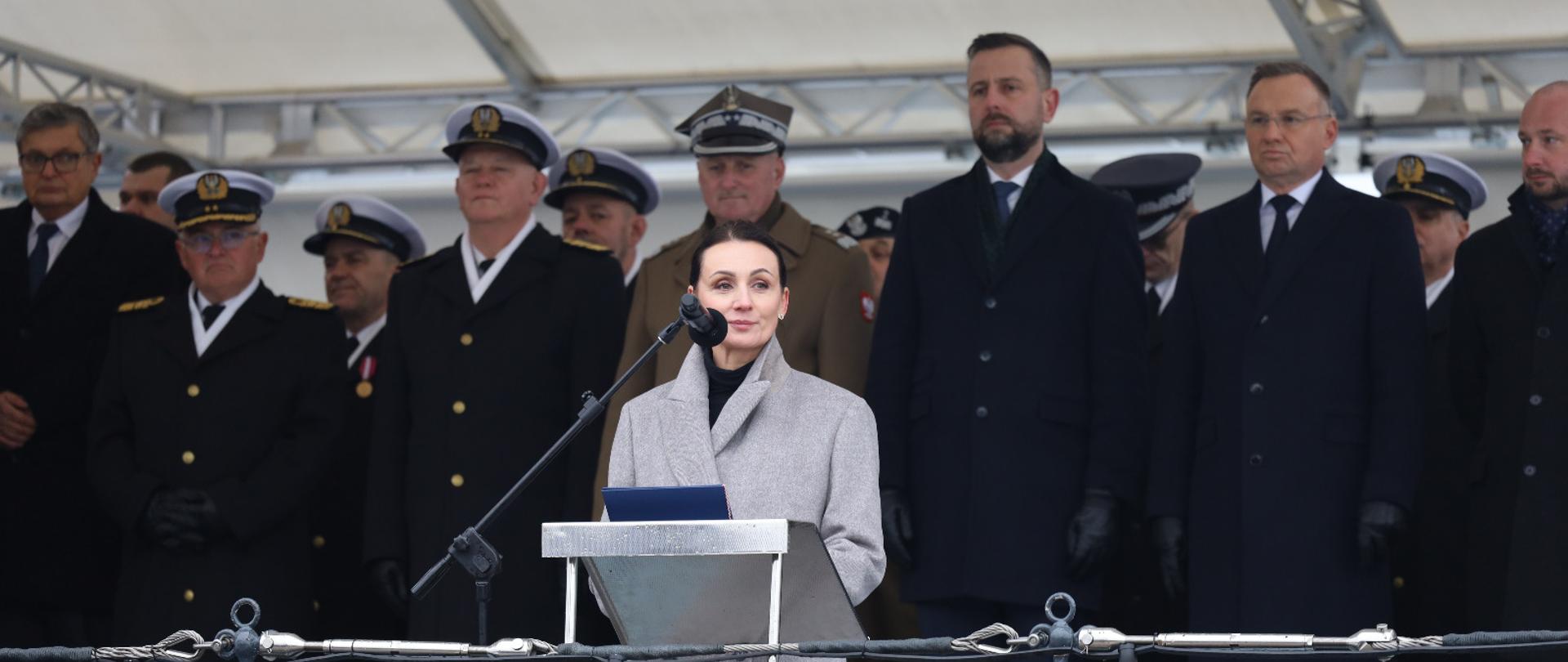 Kobieta (wojewoda pomorska) stoi na pokładzie okrętu ORP Błyskawica i przemawia. Za nią stoi prezydent RP i minister obrony