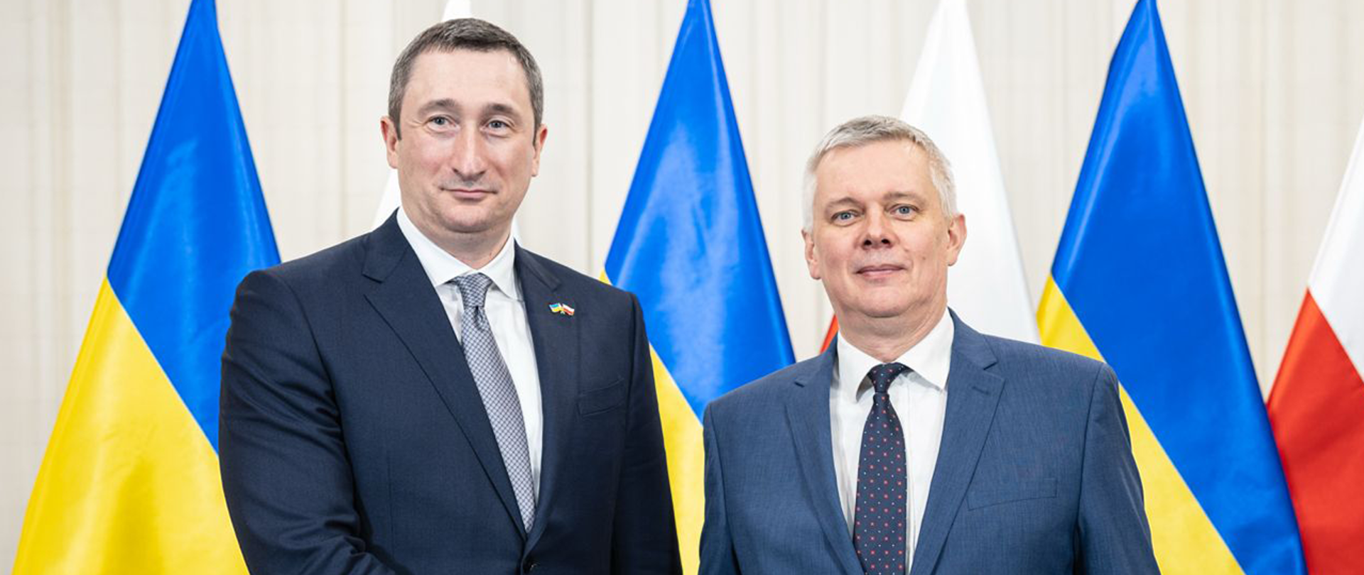 The ministers stand against the background of Polish and Ukrainian flags.