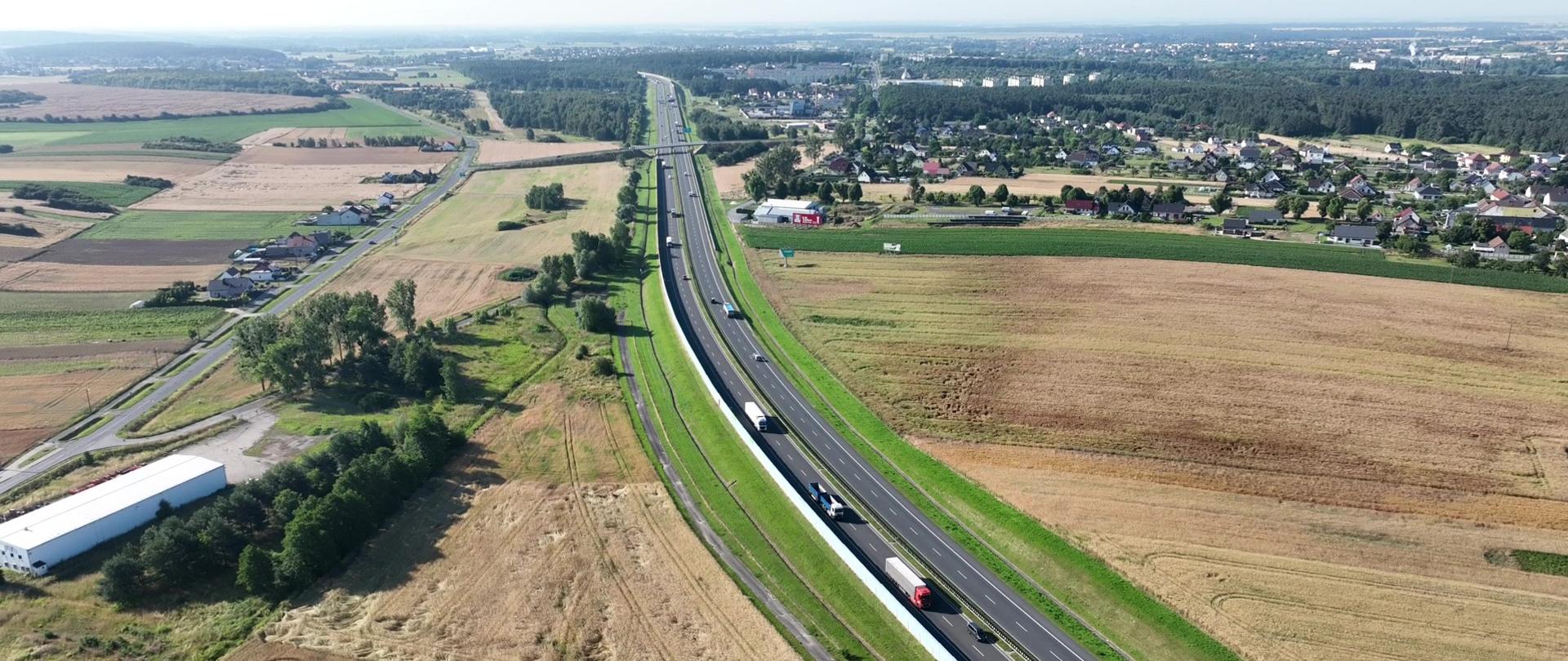 Fragment opolskiego odcinka autostrady A4 na wysokości miejscowości Odrowąż, ruch pojazdów ciężarowych i osobowych w obu kierunkach, w tle panorama Opolszczyzny