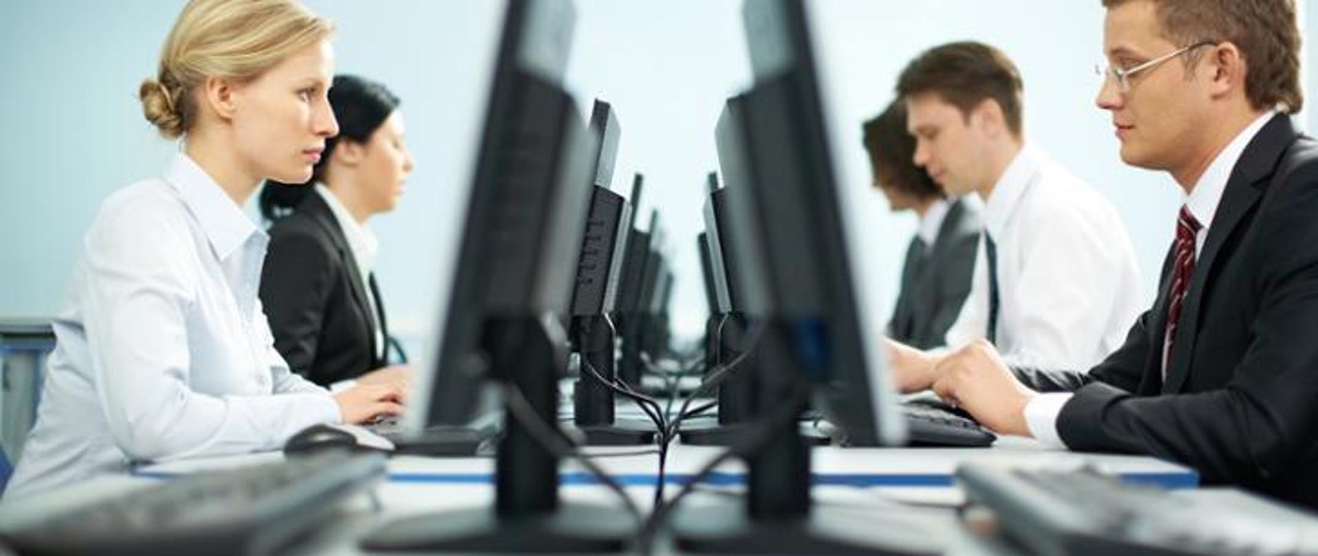 Pięciu pracowników biurowych siedzących naprzeciwko siebie, którzy pracują przed komputerami 