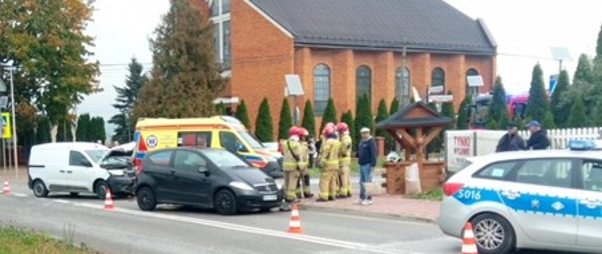 Zdjęcie przedstawia miejsce wypadku: z lewej strony dwa uszkodzone auta, z prawej stoi radiowóz