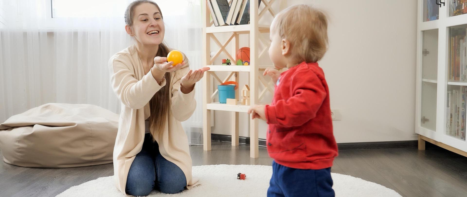 Happy cheerful mother laughing at her little baby son making first steps at home. Baby development, family playing games, making first steps, parenthood and care.