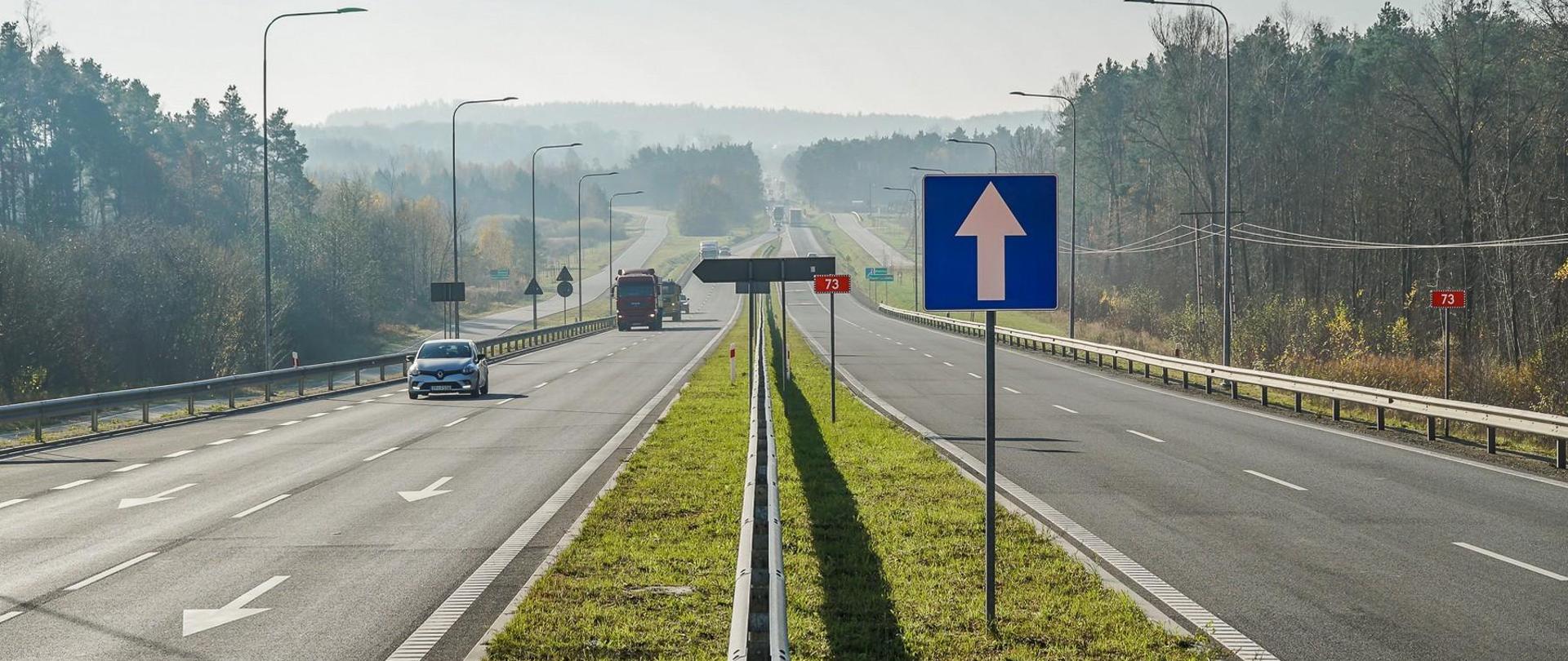 Obwodnica Morawicy etap I - dwujezdniowa droga, jadące samochody, znaki drogowe i tablice m.in. z numerem drogi 73