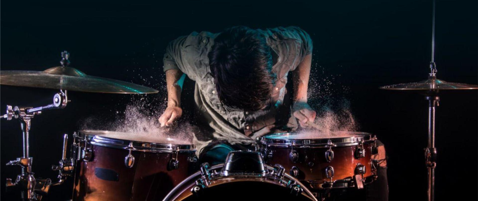 Plakat reklamujący koncert w wykonaniu uczniów klasy perkusji. Na plakacie zdjęcie osoby grającej na zestawie perkusyjnym na ciemnym tle.