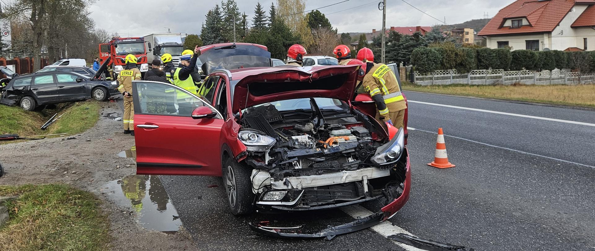 Zdjęcie przedstawia miejsce wypadku:: na pierwszym planie zniszczone auto hybrydowe, a z lewej strony drugi z uszkodzonych aut.