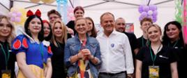 Pod namiotem Minister Nowacka i Premier Tusk pozują do zdjęcia wśród osób przebranych za postacie z bajek.