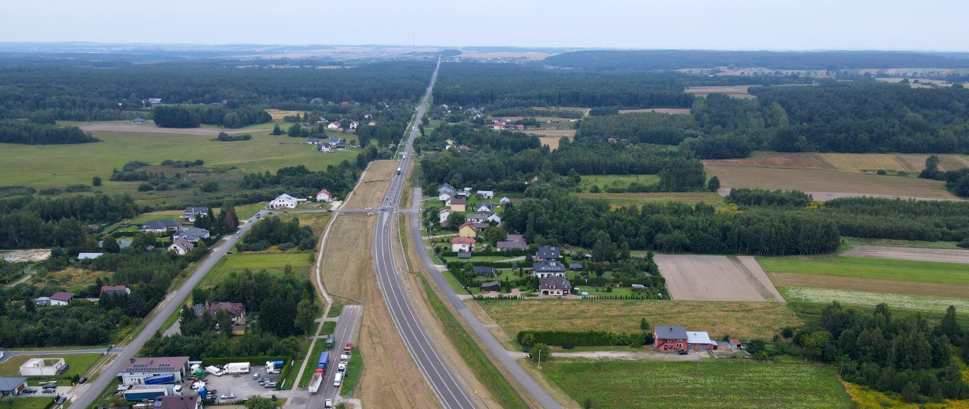 Zdjęcie lotnicze drogi krajowej DK17 w okolicach Zamościa i Tomaszowa Lubelskiego. Droga krajowa ciągnąca się po horyzont przechodząca w okolicach zabudowań i przechodząca przez lasy i łąki.