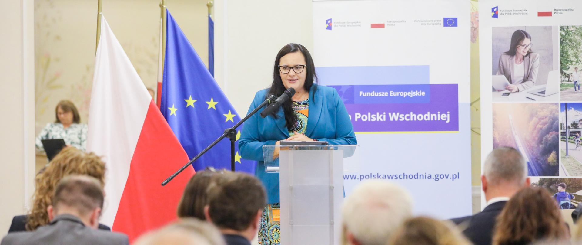 W sali konferencyjnej w mównicy z mikrofonem wiceminister Małgorzata Jarosińska-Jedynak. Przed nią publiczność. Za nią flagi PL i UE oraz banery.