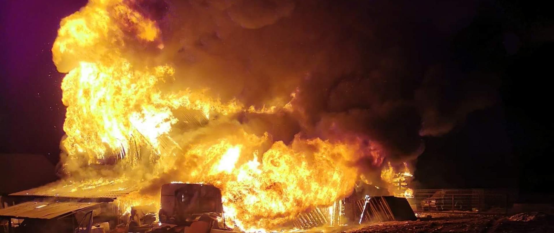 Zdjęcie przedstawia słup ognia, którym objęty jest cały budynek garażowo-warsztatowy. Zdjęcie zrobione w porze nocnej.