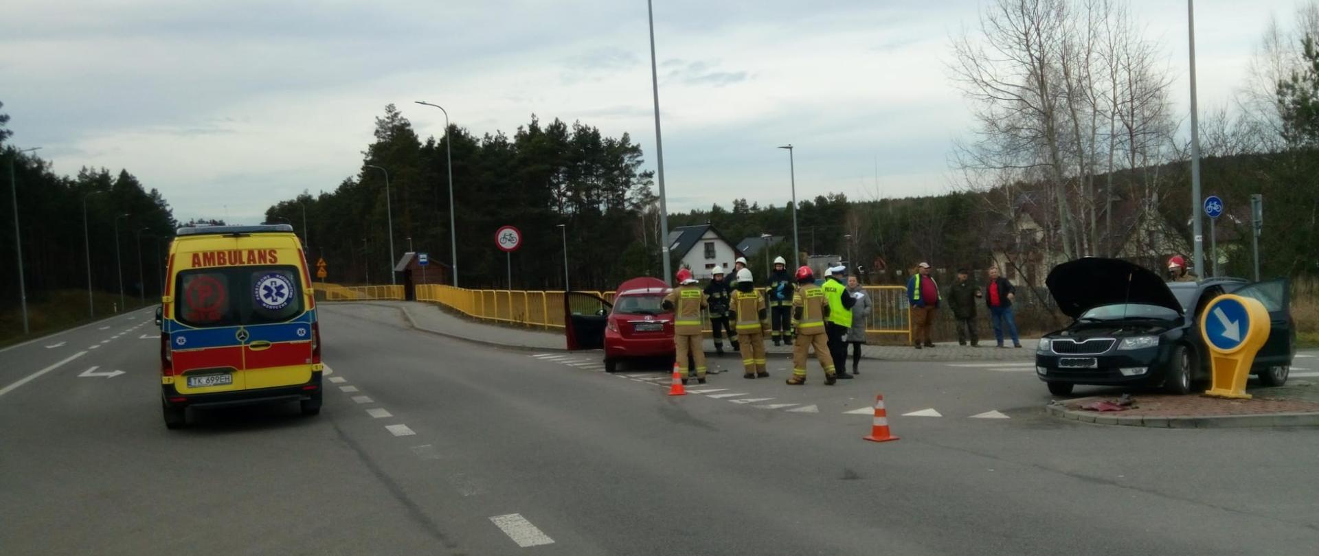 Zdjęcie przedstawia miejsce wypadku: widać dwa uszkodzone auta, a z lewej strony stoi ambulans.