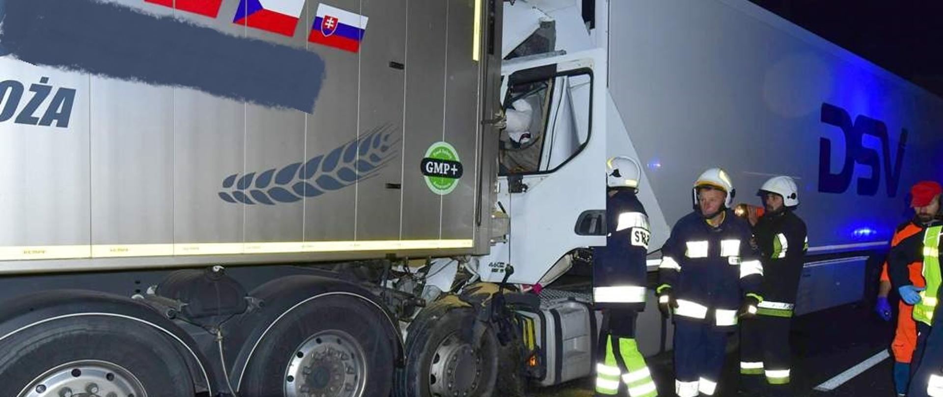 Na zdjęciu zmiażdżona kabina samochodu ciężarowego, który uderzył w stojący przed nim ciągnik siodłowy z naczepą oraz strażacy ze sprzętem hydraulicznym prowadzący działania związane z uwolnieniem zakleszczonego kierowcę.