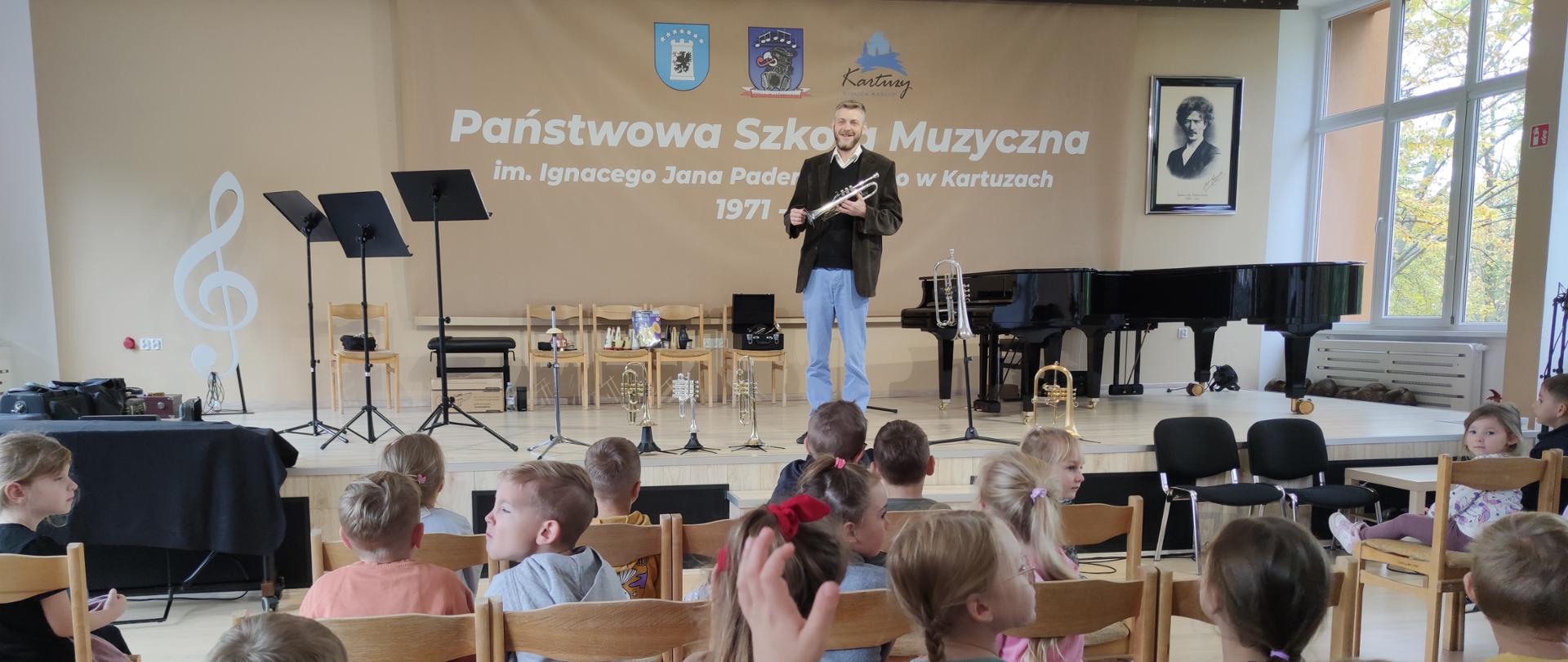 na scenie nauczyciel z trąbką przemawiający do przedszkolaków