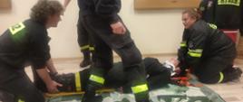 Na zdjęciu widoczni strażacy ratownicy OSP, wykonujący badanie urazowe poszkodowanego.
