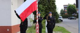 Widok z przodu. Poczet flagowy podczas prezentacji flagi na maszcie. Dowódca pocztu trzyma rozpostartą flagę Polski. Asystujący salutuje. 