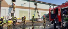 Strażacy prowadzący działania ratowniczo – gaśnicze na zewnątrz hali magazynowej