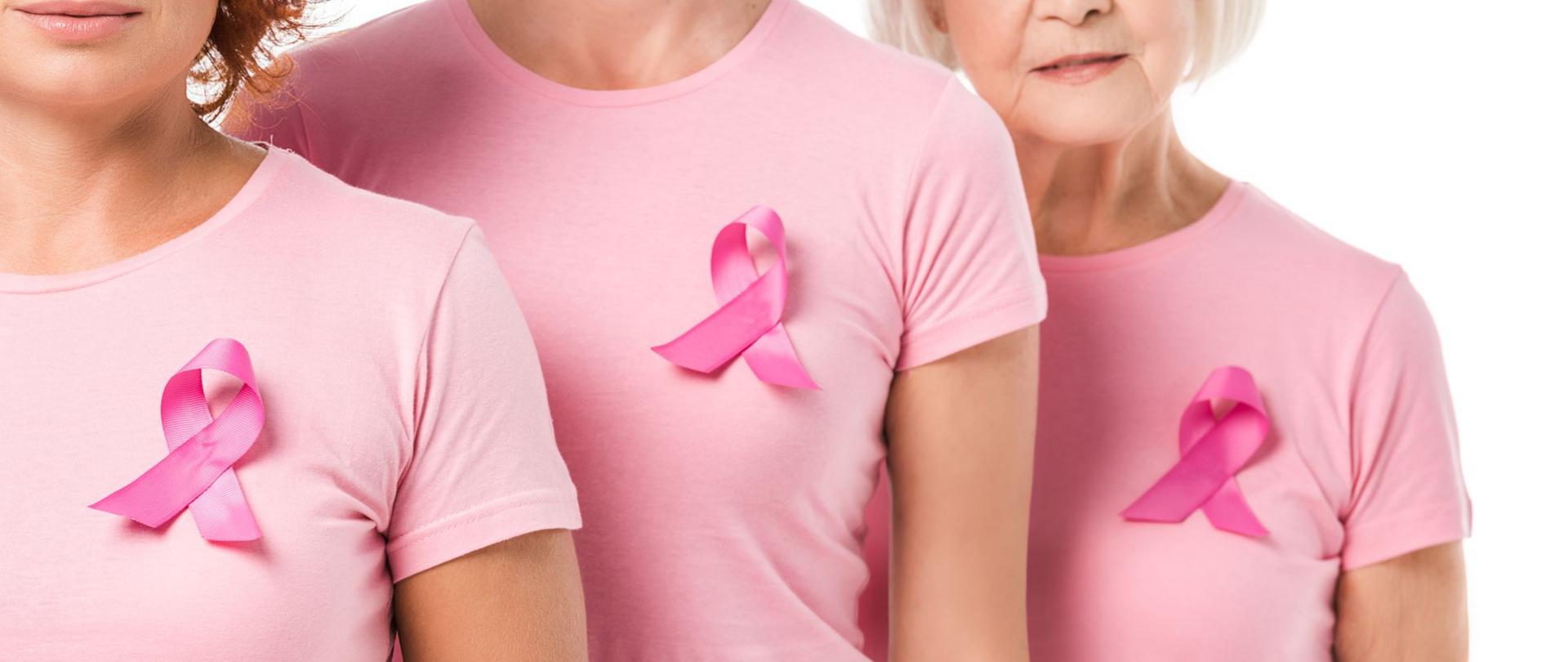 Na zdjęciu są widoczne trzy kobiety ubrane w różowe koszulki, na których są przyczepione różowe wstążki.