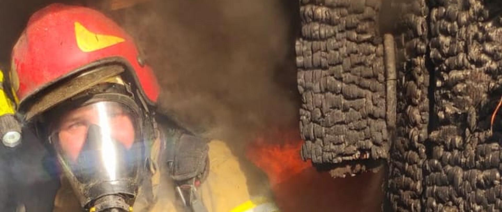 Strażak w ubraniu bojowym i sprzęcie ochrony dróg oddechowych wychodzi ze spalonego budynku