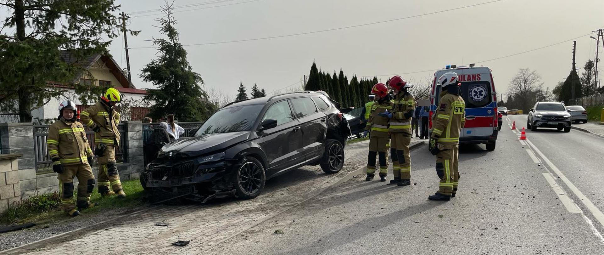 Zdjęcie - W tle ambulans, samochód biorący udział w zdarzeniu a także strażaków pracujących na miejscu zdarzenia.