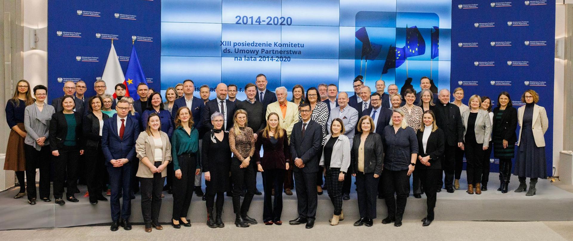 Grupa osób stoi w trzech rzędach na scenie. W pierwszym rzędzie w środku stoi minister Katarzyna Pełczyńska-Nałęcz.