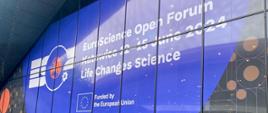 Widok na przeszkloną ścianę budynku z napisem EuroScience Open Forum.