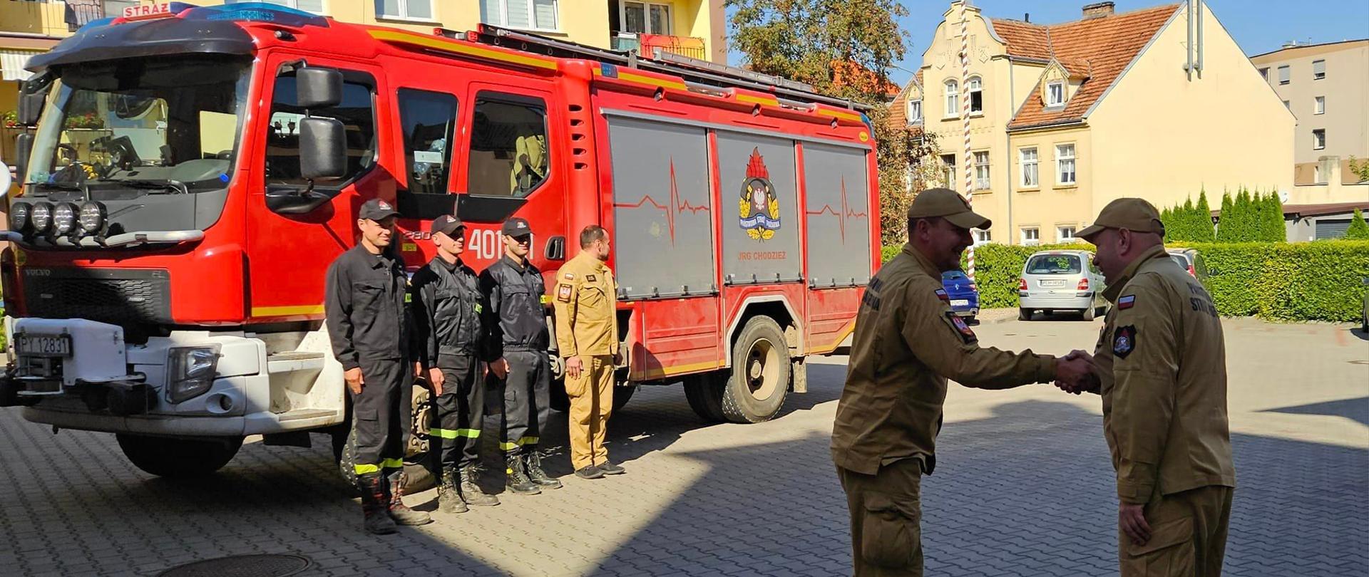 Zdjęcie przedstawia strażaków , którzy wrócili z działań przeciwpowodziowych z południa polski.
W tle samochód strażacki oraz budynki.
