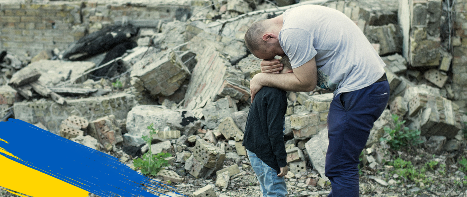 A man hugs a boy. Ruins of a building in the background 