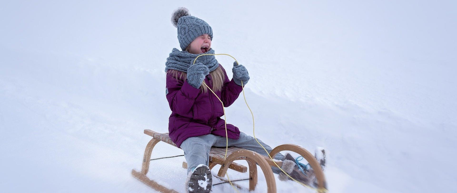 Dziewczynka zjeżdżająca na sankach z zaśnieżonej górki