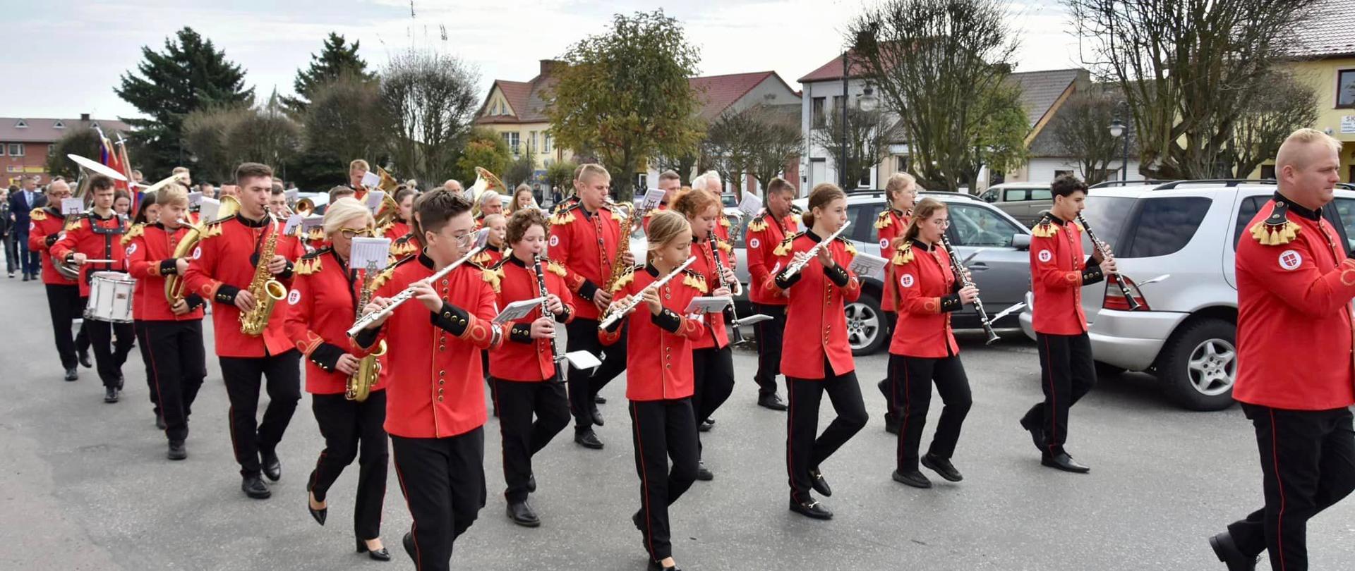 Orkiestra przemieszcza się ulicą miasta. Każdy trzyma w dłoni instrument muzyczny. 