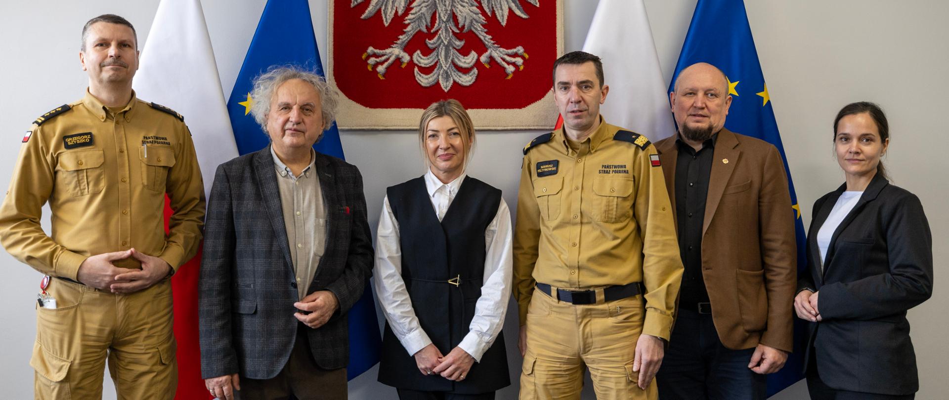 Grupa sześciu osób na tle godła Polski i flag Polski i UE.