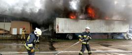 Na zdjęciu widać płonącą naczepę od tira oraz strażaków prowadzących działania gaśnicze.