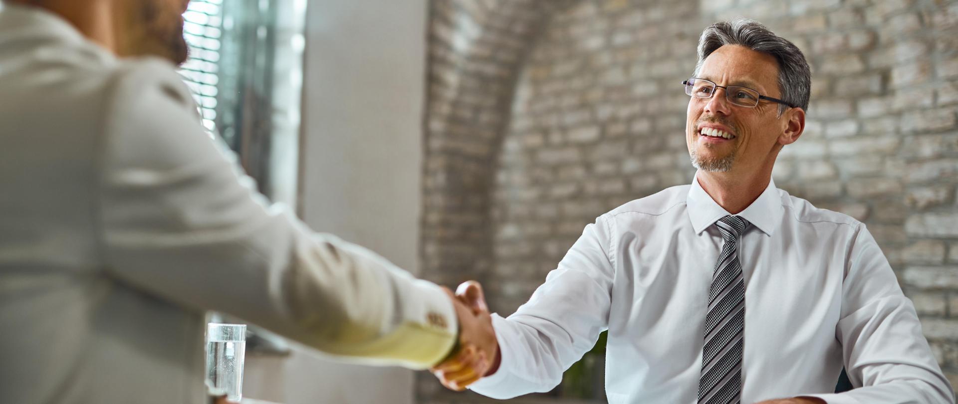 Happy manager handshaking with a candidate after successful job interview in the office.