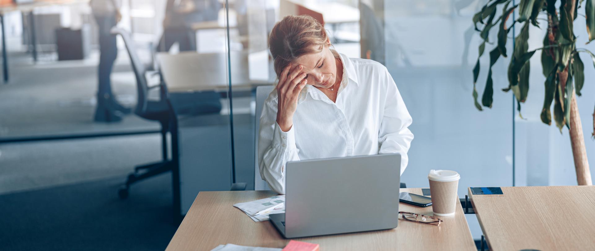 Tired businesswoman with headache working on laptop at her workplace at modern office. 