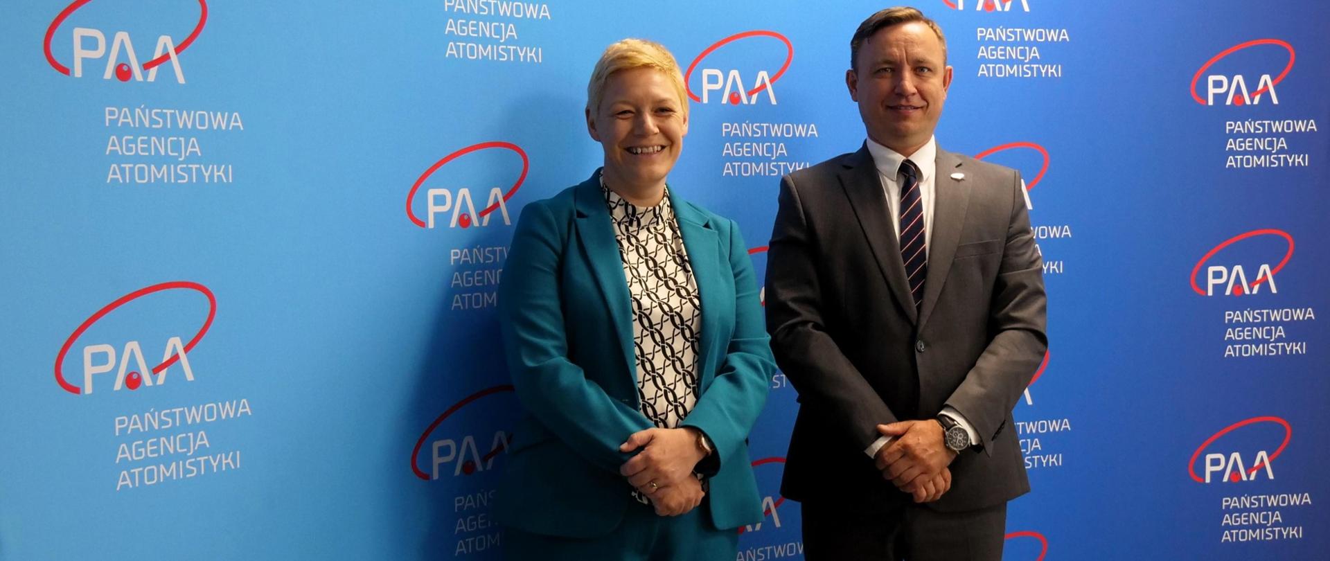 Prezes Państwowej Agencji Atomistyki Andrzej Głowacki i Jennifer Tyldesley Radcą-Minister ds. Gospodarczych w ambasadzie brytyjskiej stoją na tle ścianki z logo PAA.
