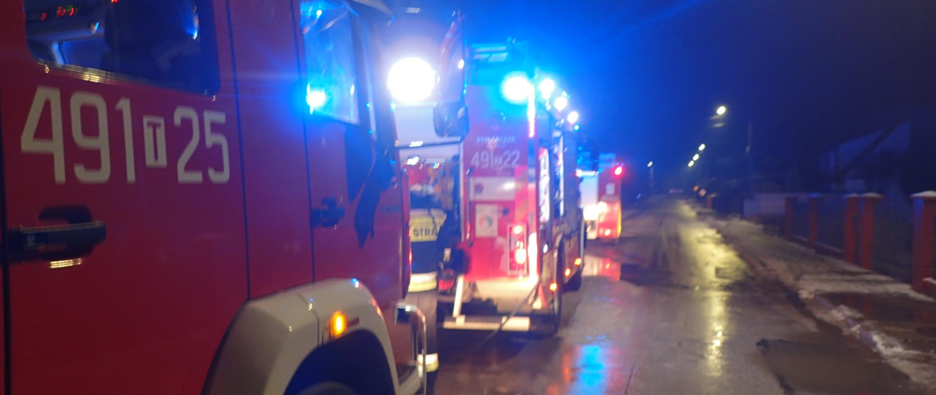 Samochody pożarnicze zaparkowane na ulicy z włączonymi sygnałami świetlnymi, pora nocna