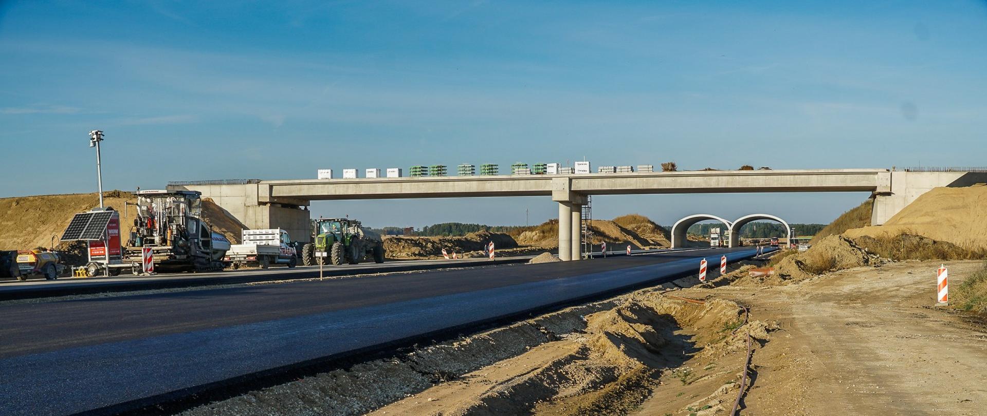 Budowa drogi S19, jest już czarna nawierzchnia, nad nią wiadukt